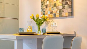 A dining area with a white table, two chairs, a vase with yellow flowers, and a wall art piece.