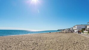 A beach with a clear sky, a sandy shore, and buildings along the coastline.