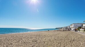 A beach with a clear sky, a sandy shore, and buildings along the coastline.