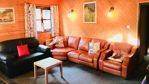 A cozy room with wooden walls and a sloped ceiling. There are two sofas, one black and one brown leather, with a small wooden table in the center. - Goldcrest 3 Hot Tub (Carmarthen)