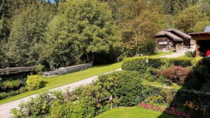 Un jardin bien entretenu, agrémenté de diverses plantes et fleurs, un sentier en bois et un bâtiment rustique doté d’un toit en pente.