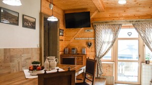 Una cabaña acogedora de madera con comedor, que incluye una mesa de madera, sillas y un televisor montado en la pared.