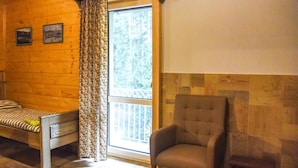 Una habitación de cabaña de madera con una cama, una silla y una ventana con cortinas.