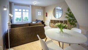 Una sala de estar moderna con un sofá, una mesa redonda con sillas, un espejo grande y una planta en maceta.