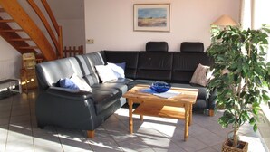 A living room with a black leather sofa, a wooden coffee table, and a potted plant.