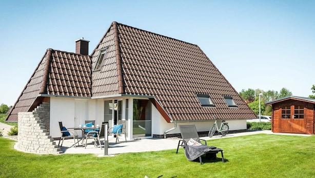 Ein Haus mit geneigtem Dach, einem Steinfundament und einer kleinen Veranda mit Sitzgelegenheiten.
