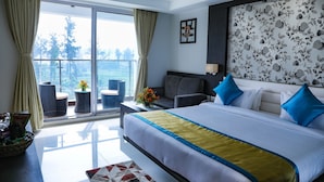 A modern hotel room with a large bed, a sofa, a balcony with wicker chairs, and a view of the outdoors. - Cygnett Inn Sea View (Kanthi)