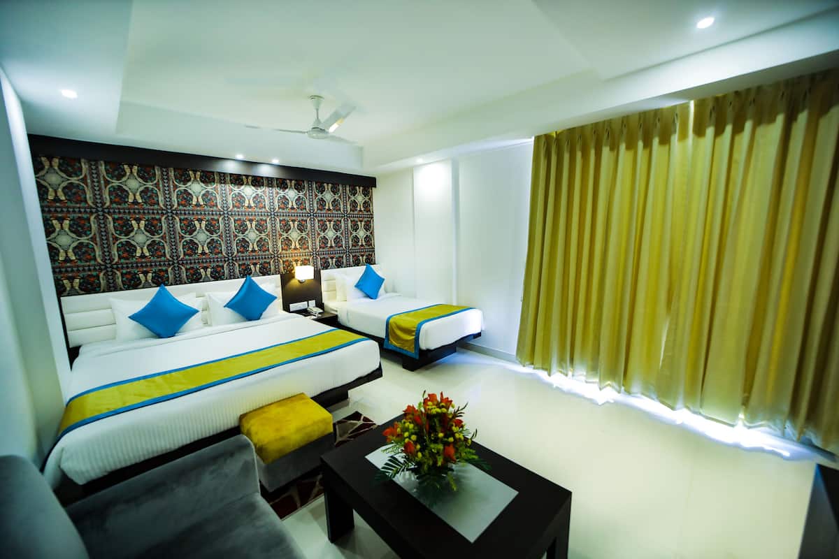 Una habitación de hotel con una cama grande, una cama más pequeña, un sofá, una mesa de centro con flores y un papel tapiz estampado.