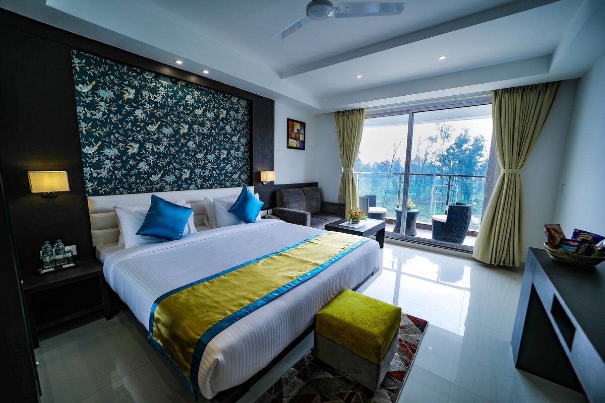Habitación de hotel moderna con una cama grande, un sofá, una mesita y un balcón con vistas.