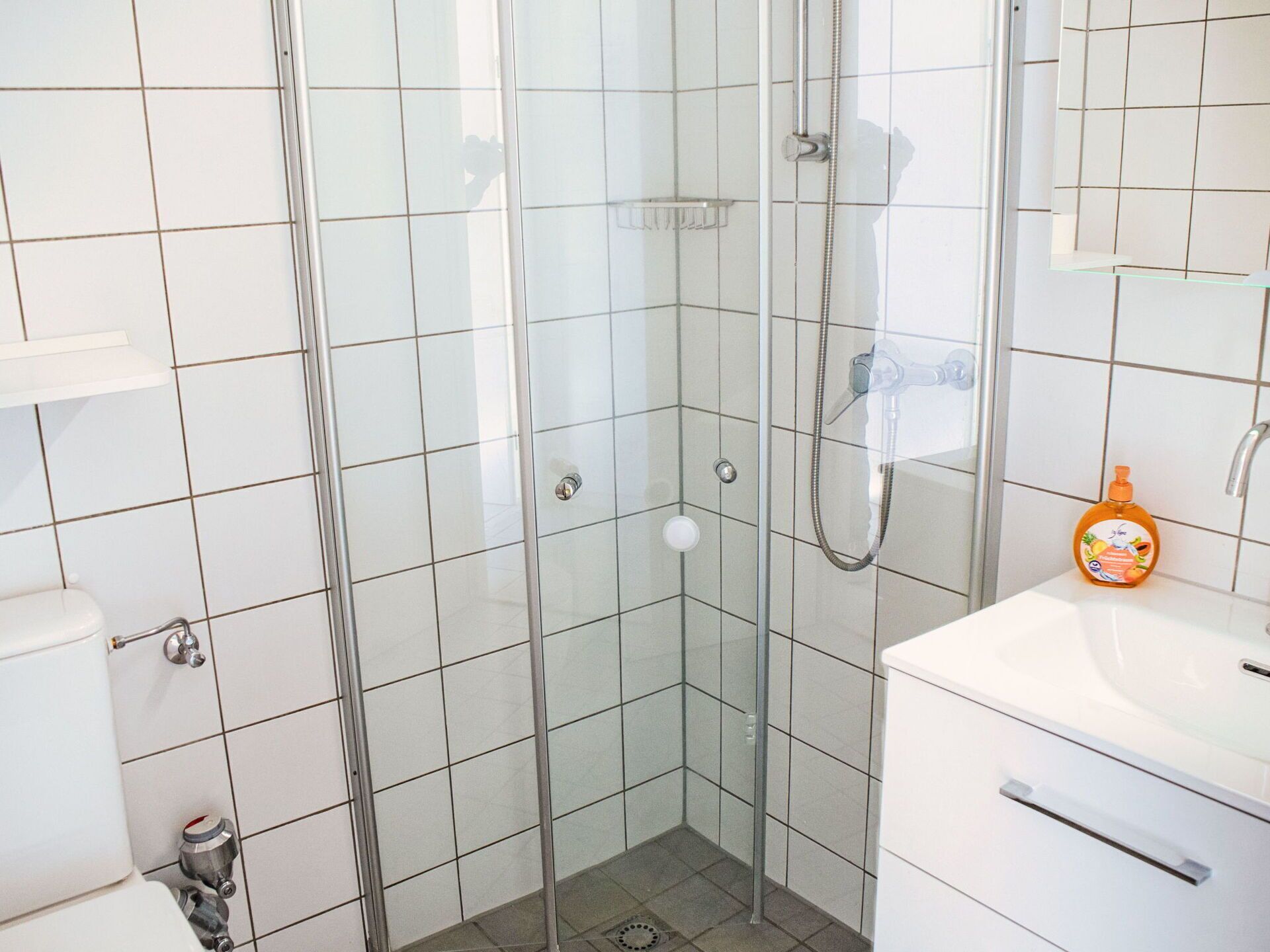 A modern bathroom with a glass-enclosed shower, white tiles, a white sink, and a mirror.