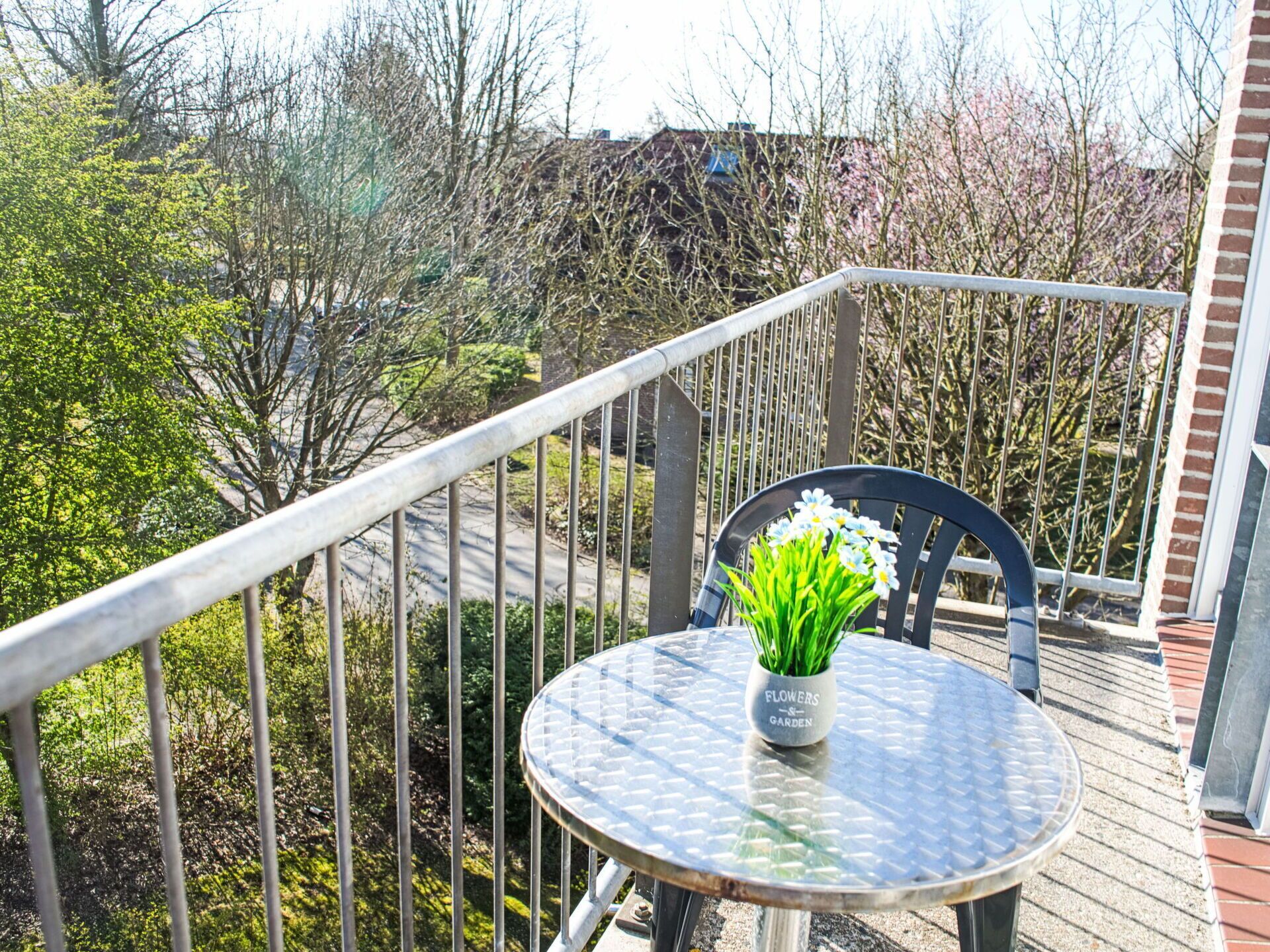 A balcony with a round metal table and a chair, a potted plant with green leaves, and a metal railing.