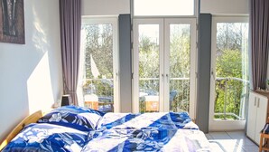 A bedroom with a bed, a wardrobe, and a balcony with a view of trees.