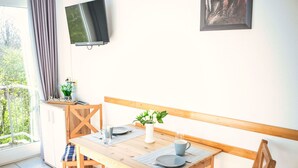 A dining area with a wooden table, chairs, a television mounted on the wall, and a window with curtains.