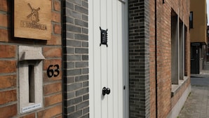 Un edificio de ladrillo con una puerta blanca, una placa de madera con un molino y un buzón con el número 63.