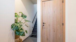 Un pasillo con una puerta de madera, una escalera y una planta en maceta.