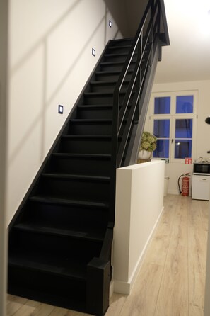 A modern staircase with black steps and a glass railing, leading to a room with a wooden floor and a white wall. - B&B De Hoogmolen (Bruges)