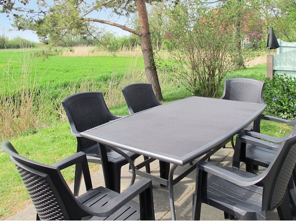 Relax on the patio surrounded by lush greenery and enjoy meals at the metal table with comfortable seating.