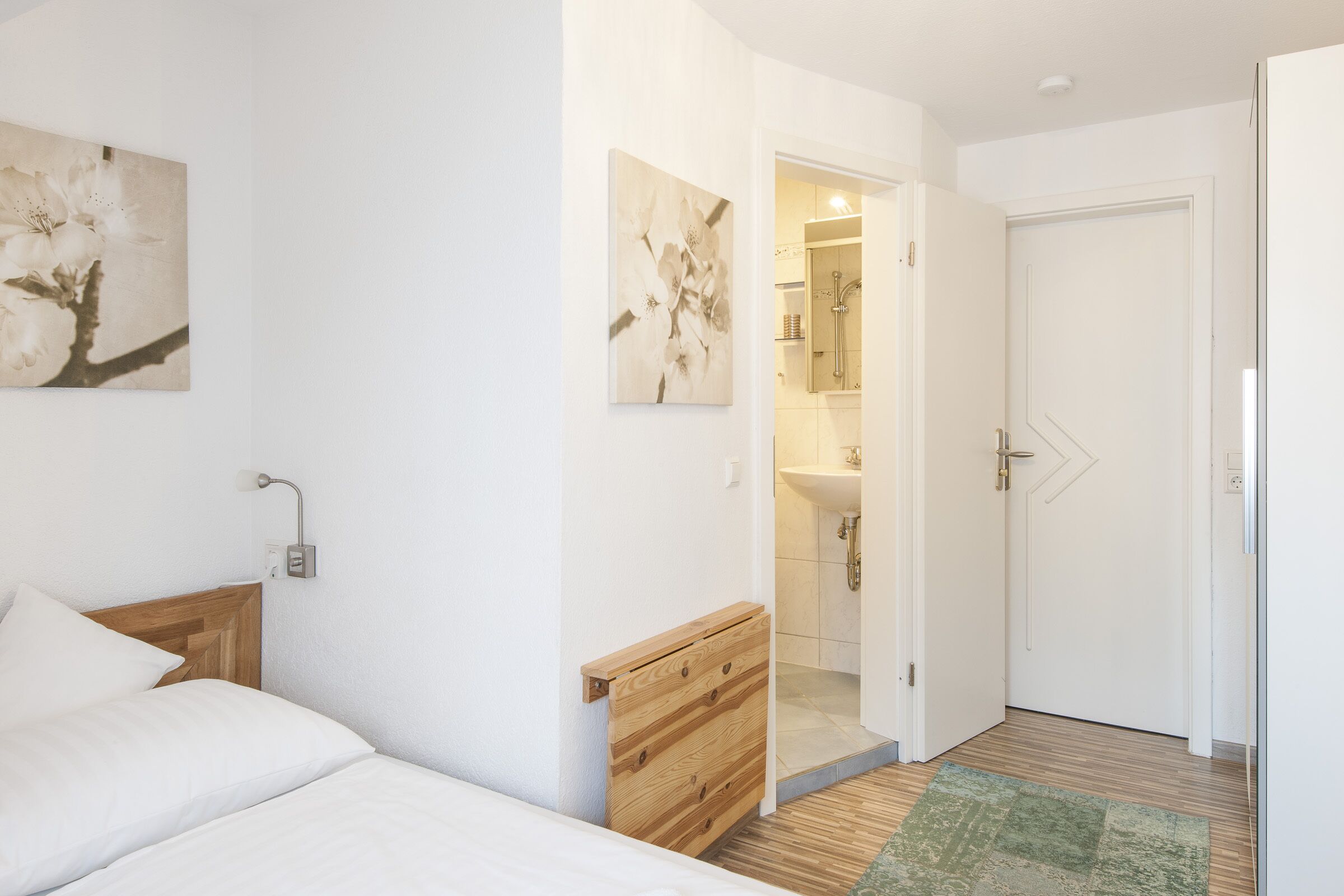 Ein Schlafzimmer mit einem Holzkopfteil, einem Bett mit weißer Bettwäsche, einem grünen Teppich und einer hölzernen Kommode.