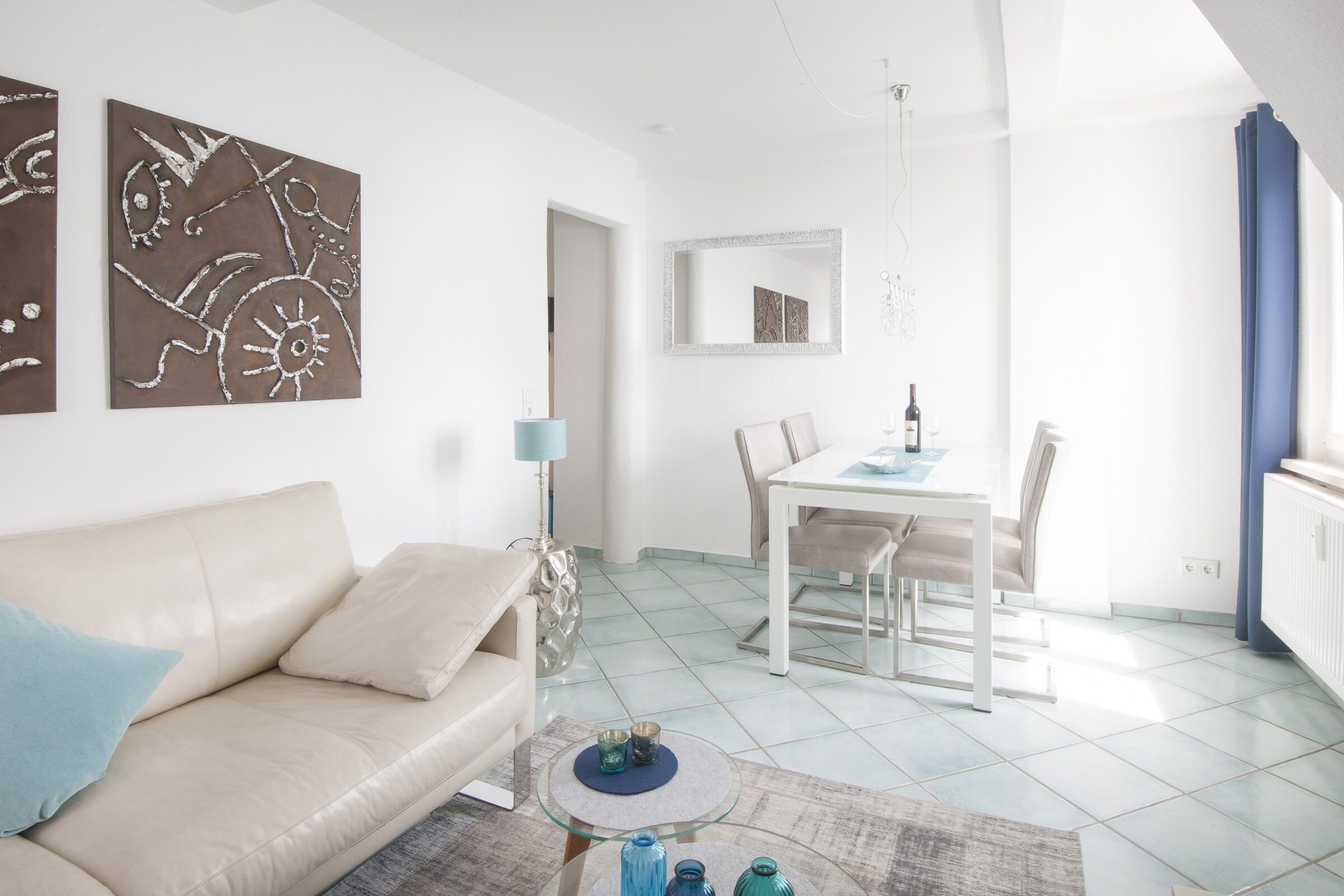 Ein modernes Wohnzimmer mit einem beigefarbenen Sofa, einem Glastisch und abstrakter Wandkunst.