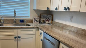 A kitchen with white cabinets, a stainless steel dishwasher, and a countertop with a crab-themed sign. - Waterfront home w/dock-Jon boat, Kayaks & fishing poles included! (Port Richey)