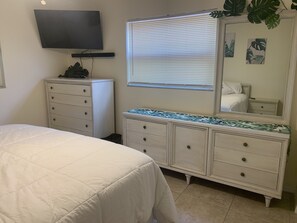 A bedroom with a bed, dresser, television, and window with blinds.