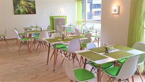 A dining area with tables and chairs, a radiator, and a window with curtains. - Hotel Austria Stuttgart-City (Stuttgart)