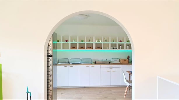 An arched doorway leading to a kitchen with white cabinets, a countertop with appliances, and a chair. - Hotel Austria Stuttgart-City (Stuttgart)