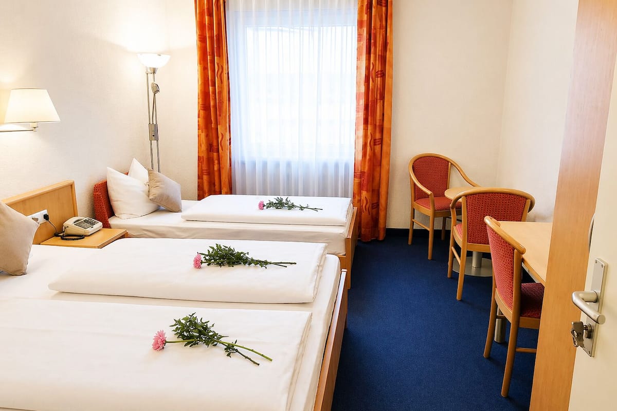 A hotel room with two beds, a desk, a chair, a lamp, and a phone on the bedside table.