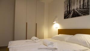 A neatly made bed with white linens and towels, a wooden headboard, and a wall-mounted light fixture. - Golte Apartments (Mozirje)