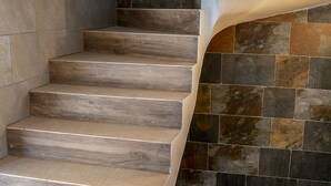 A staircase with wooden steps and a wall with multicolored stone tiles. - Golte Apartments (Mozirje)