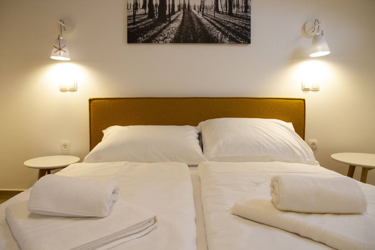 Une chambre d’hôtel avec deux lits, du linge de lit blanc et un grand tableau au mur.