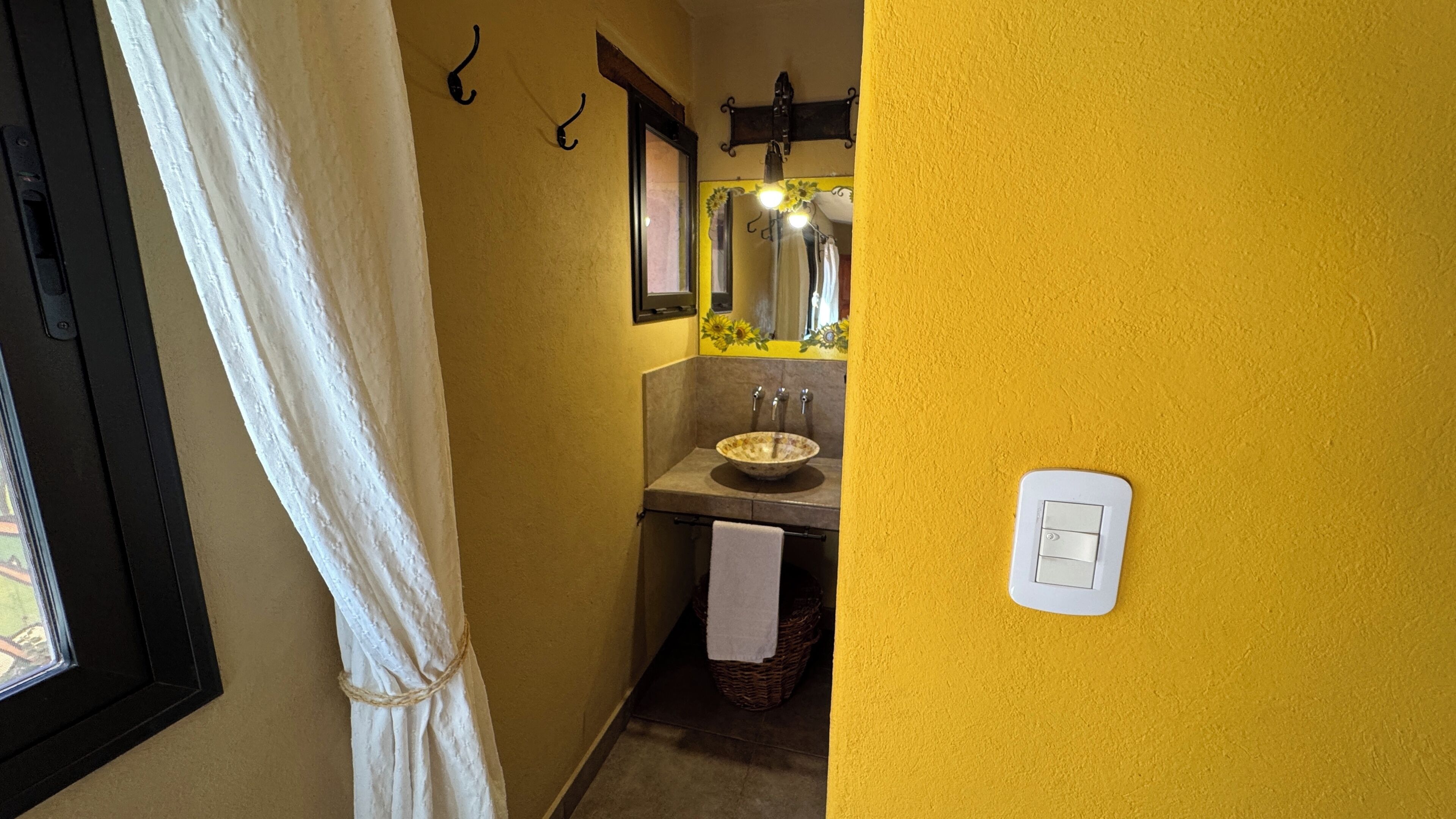 Une salle de bain avec un mur jaune, un lavabo blanc, un miroir et un porte-serviettes.