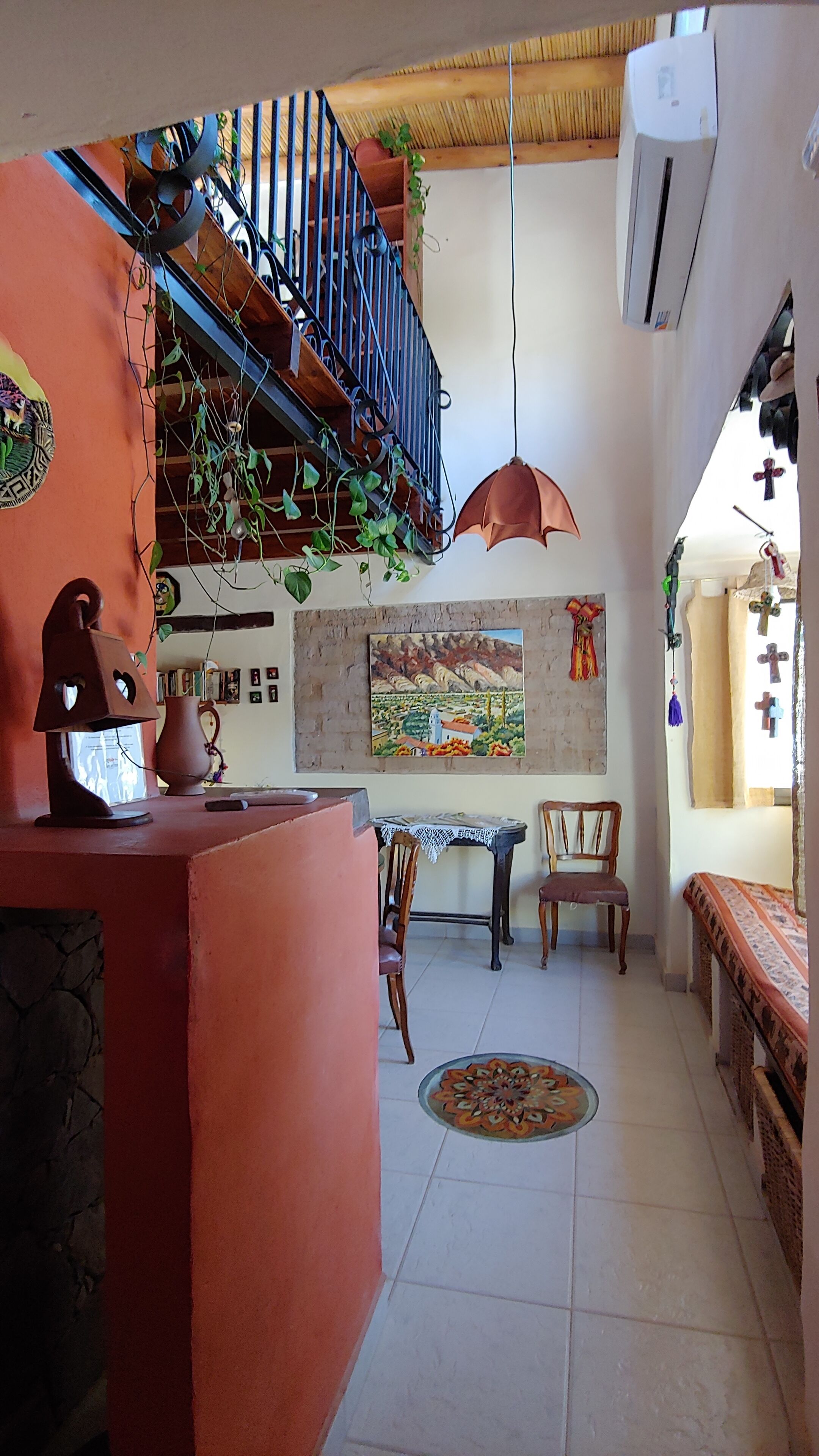 A cozy living area with a wooden staircase, a dining table with chairs, a decorative lamp, and a painting on the wall.
