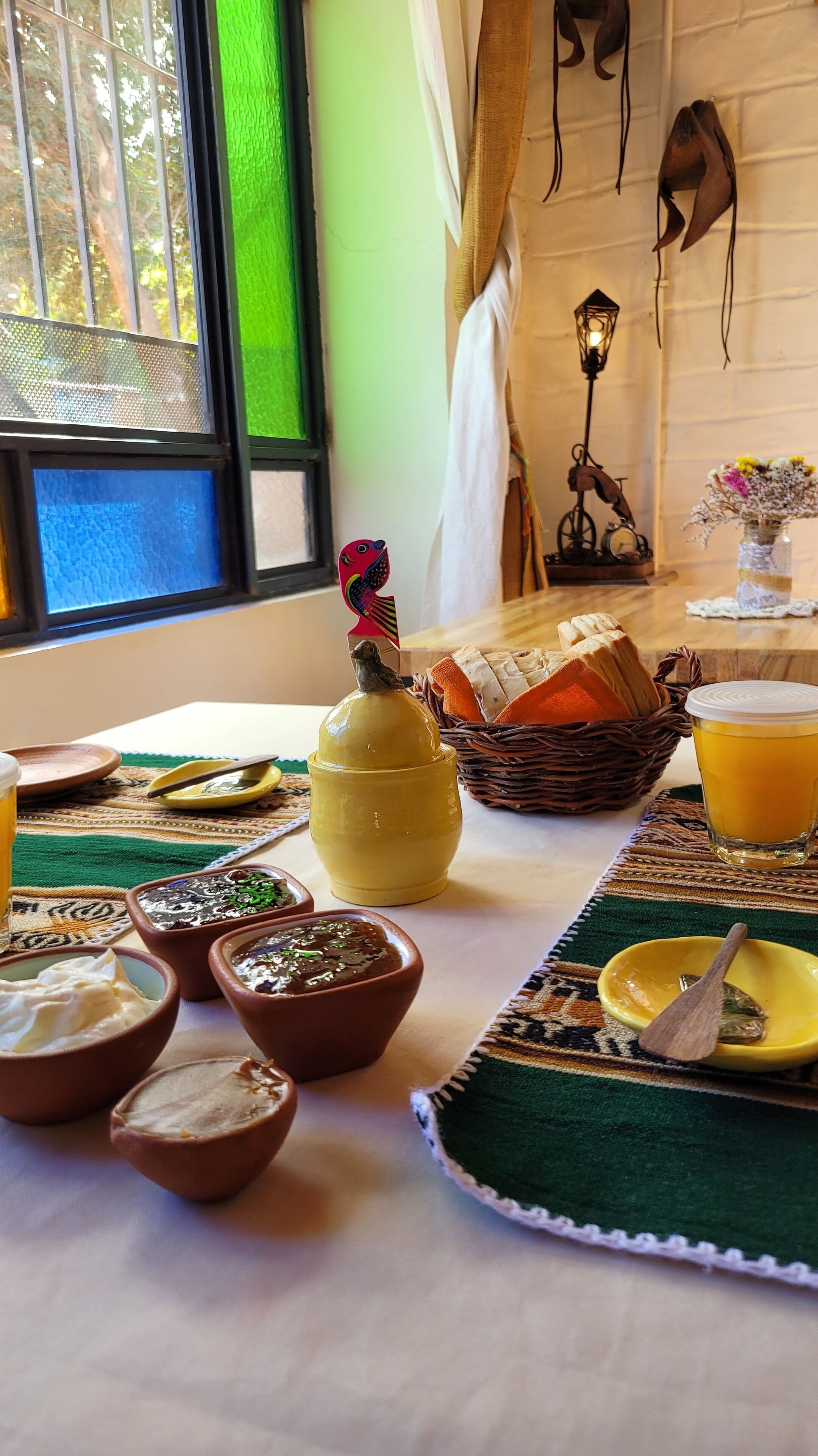 Mesa puesta con platos tradicionales, una jarrón y una cesta de pan, con vistas a la vegetación.