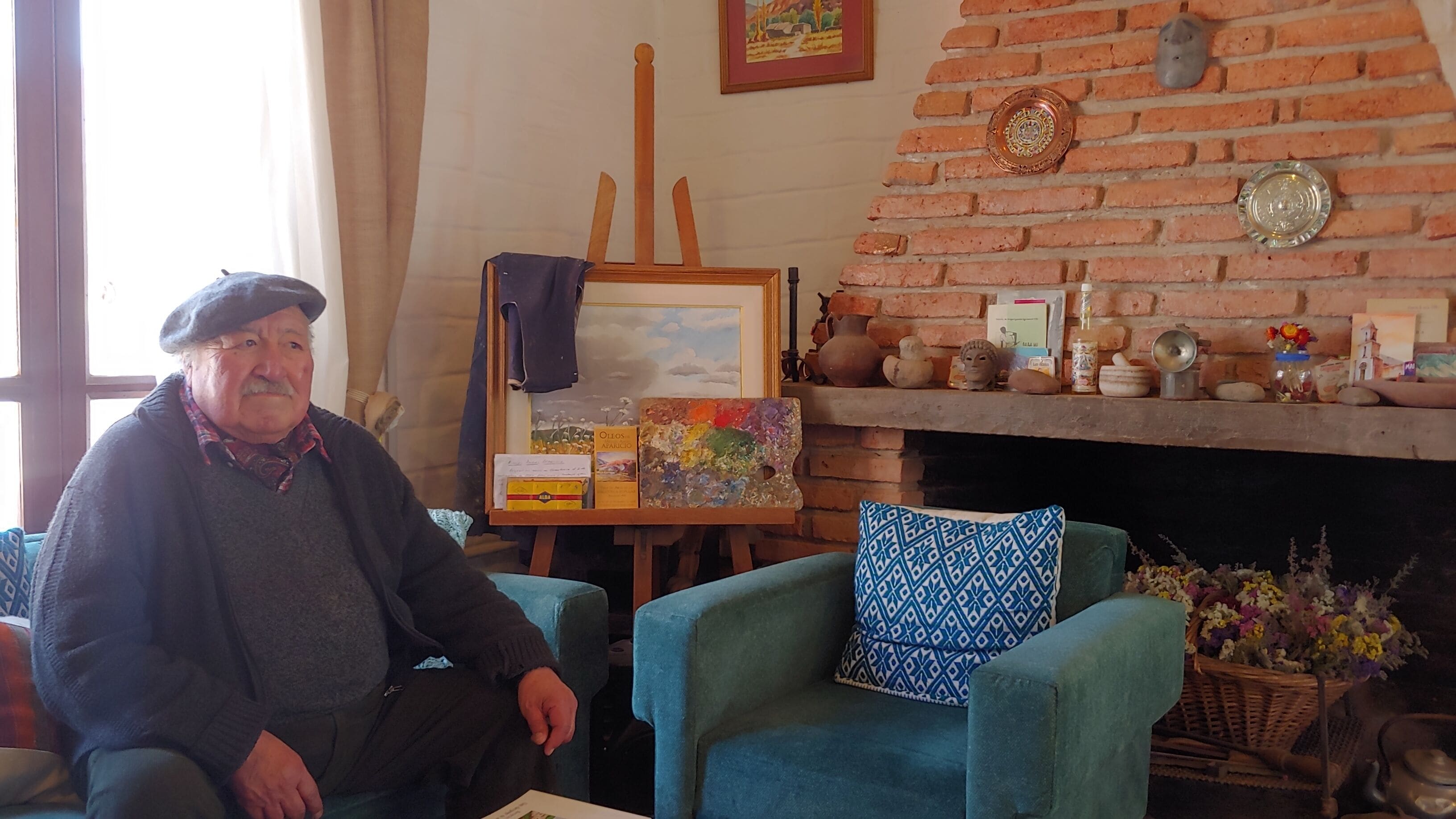 Una habitación con chimenea de ladrillo, un cuadro sobre caballete y un sillón azul.