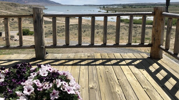 Een houten terras met een hekwerk, met uitzicht op een meer en bergen.