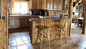 Een rustieke keuken met houten kastjes, een centraal eiland met barstoelen, en een raam dat natuurlijk licht binnenlaat.