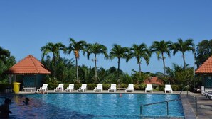 Una piscina con sillas de descanso blancas y palmeras al fondo.