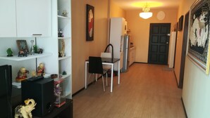 Un espacio habitable compacto con comedor, kitchenette y un pasillo que lleva a una puerta.