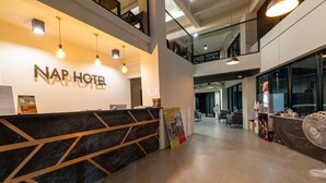 Un espace d’accueil d’hôtel au design moderne, comprenant un comptoir d’accueil, des luminaires suspendus et un escalier apparent menant à un étage supérieur.
