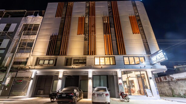 Un hôtel moderne, reconnaissable à son grand panneau « NAI », doté de nombreux espaces de stationnement et où une moto est garée à l’extérieur.