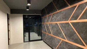 Un couloir moderne avec une porte en verre donnant sur une pièce, un mur orné d’un motif géométrique et un sol carrelé.