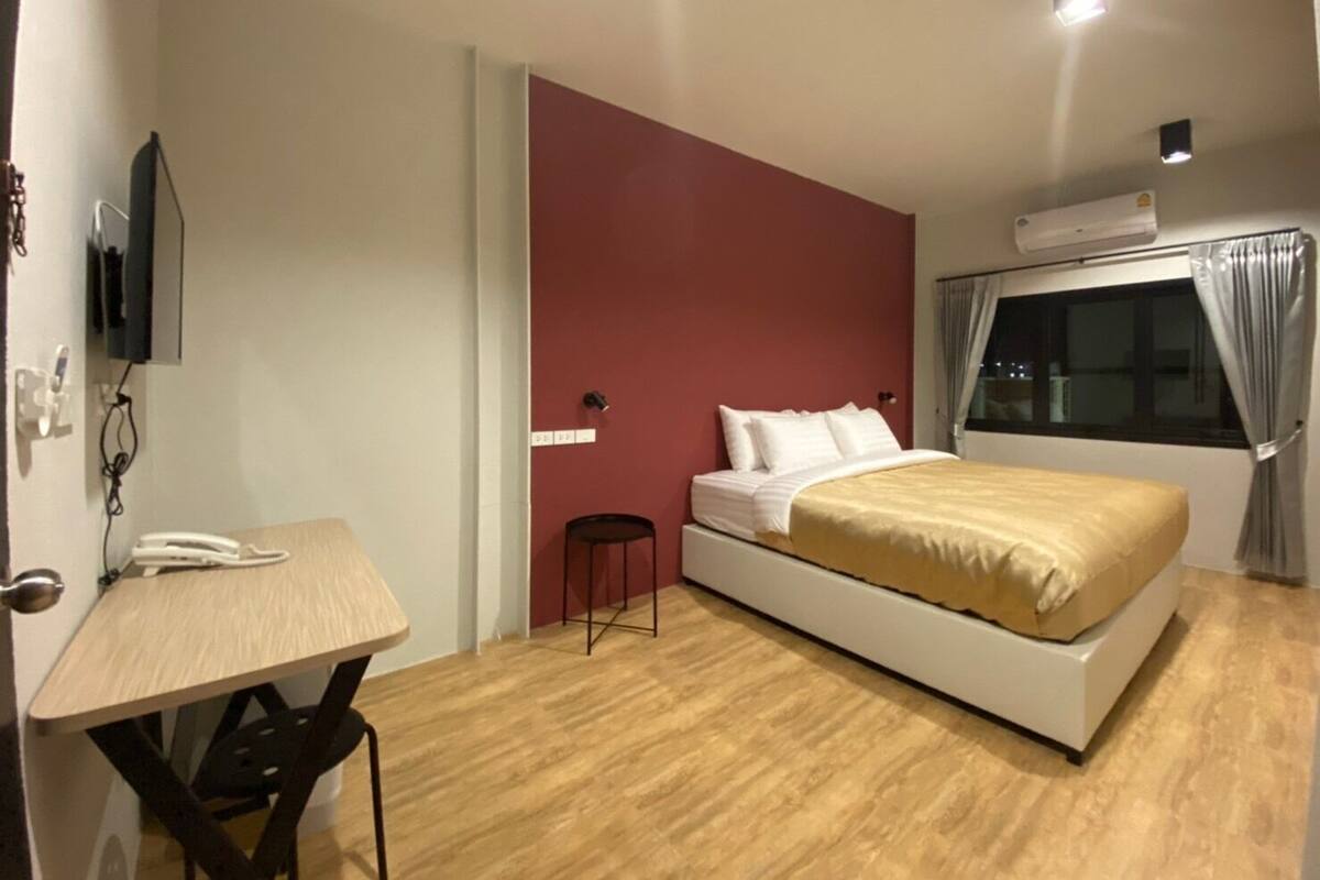 A bedroom with a bed, a desk, a chair, a TV, and an air conditioning unit.