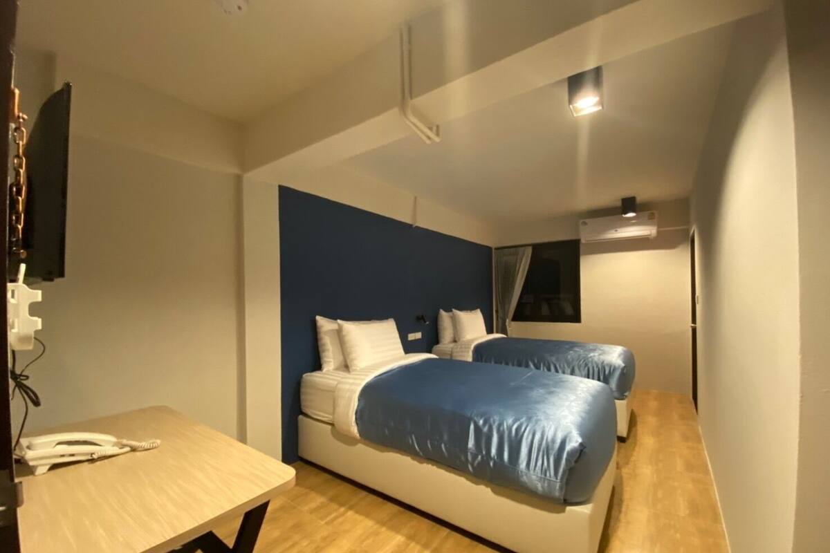 A small, modern room with two beds, a desk, and a TV.