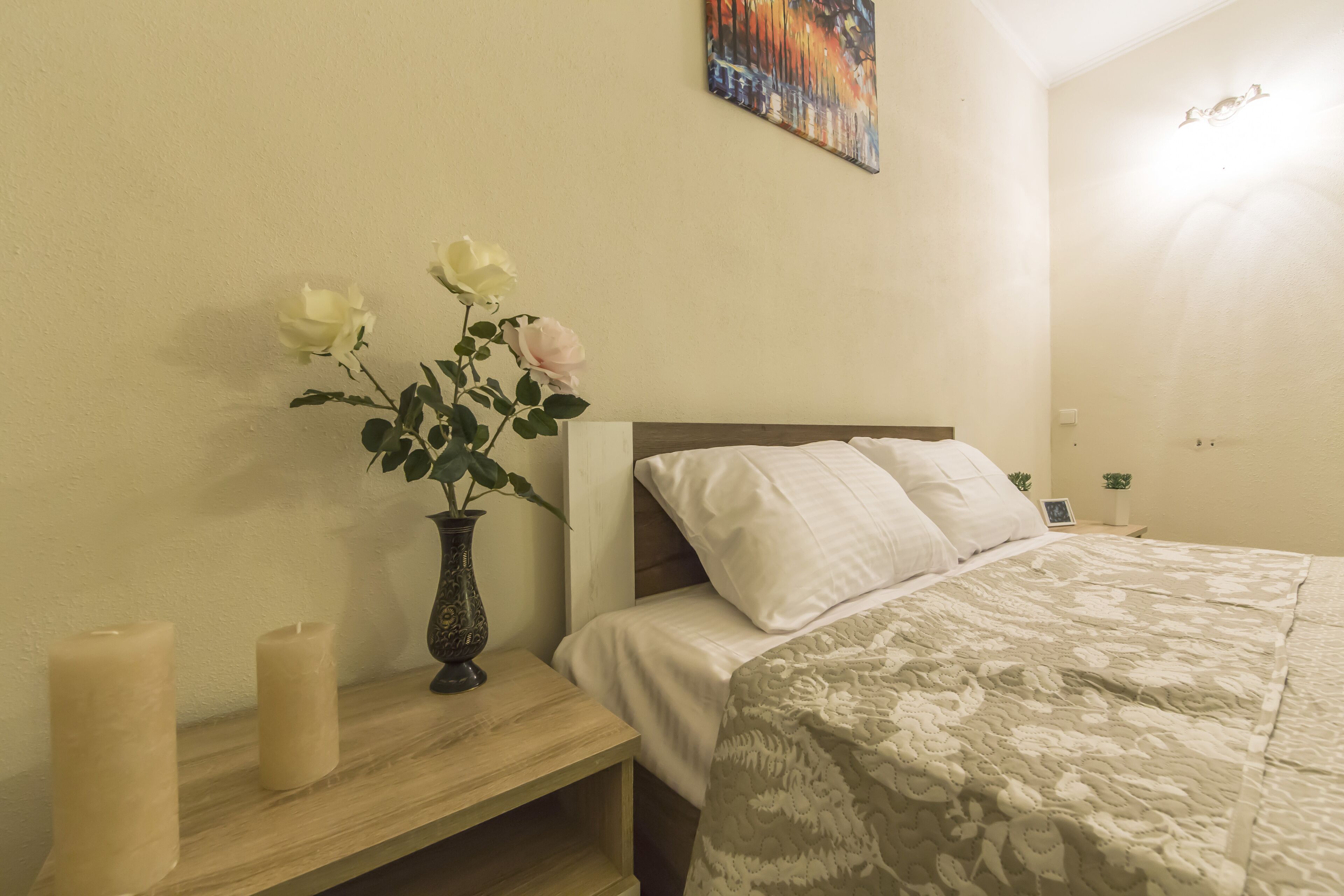 A bedroom with a bed, pillows, a bedside table with candles, and a vase with flowers.