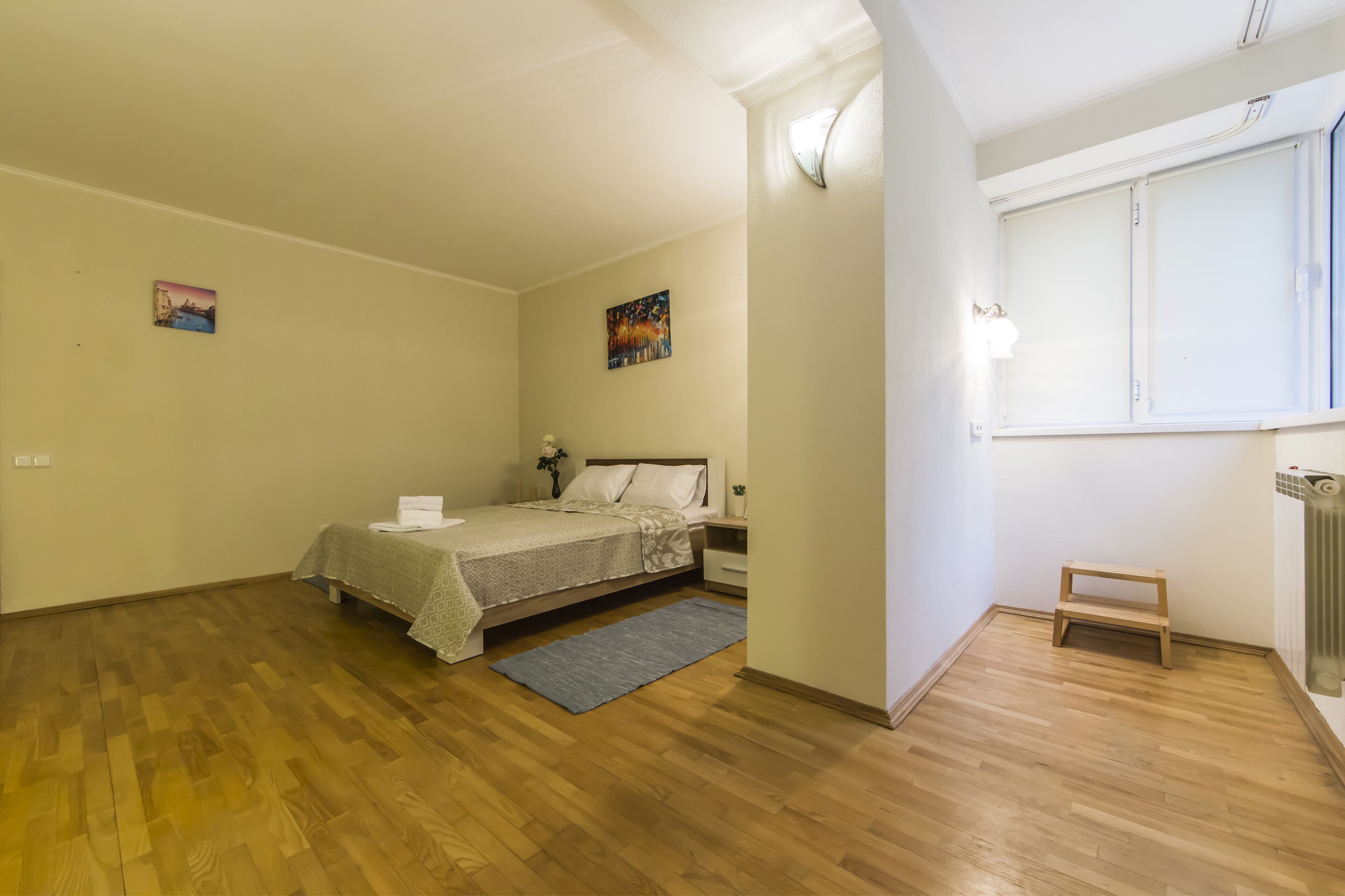 A bedroom with a bed, bedside table, lamp, and a small stool.
