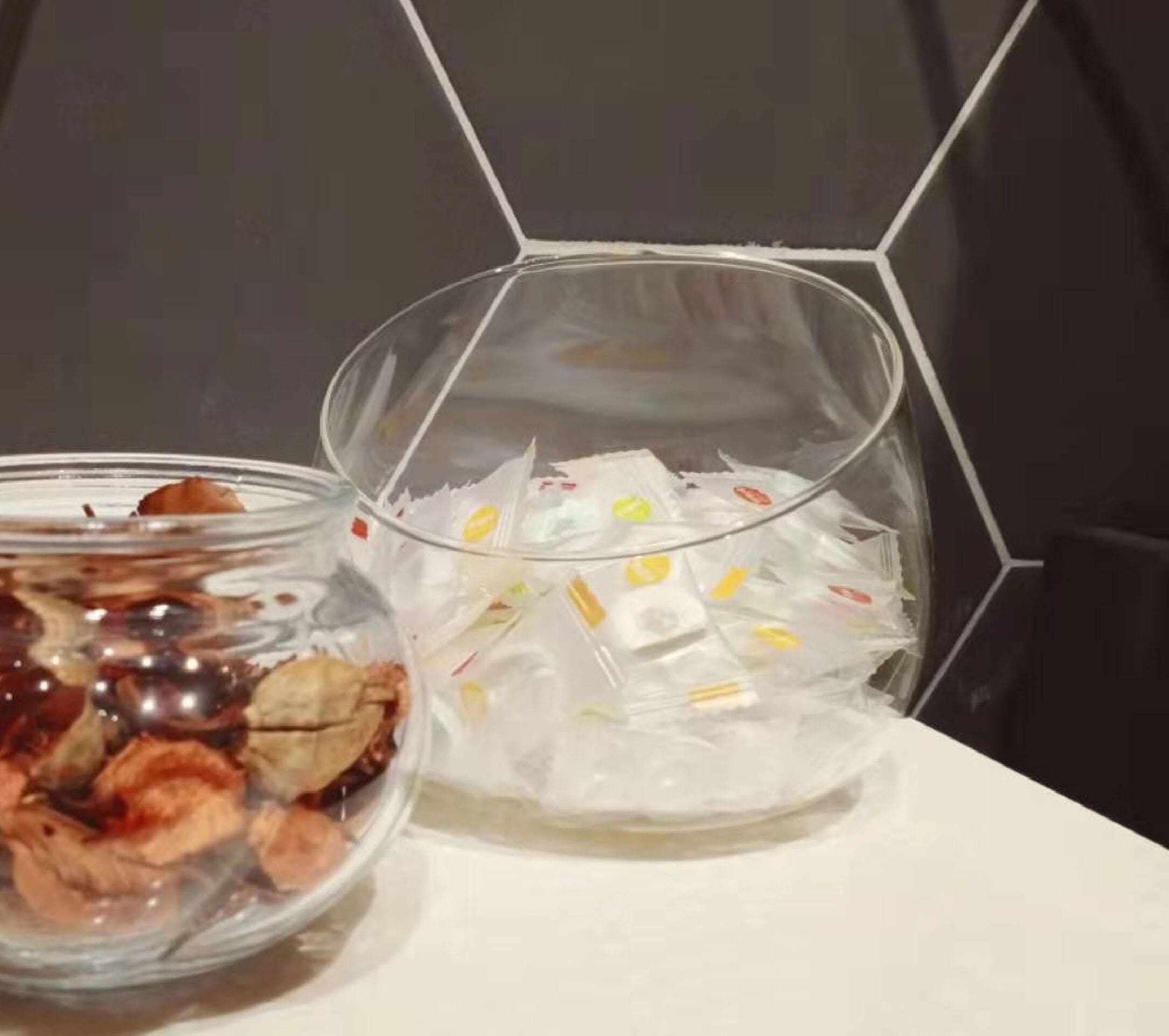 Zwei Glasglocken auf einem Tisch, eine mit Speisen, die andere mit Eiswürfeln und bunten Gegenständen.