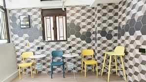 A room with a geometric patterned wall, a window with metal bars, and four chairs and tables. - The Nap Mong Kok (Kowloon)