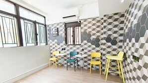 A modern interior with a geometric patterned wall, a window with metal bars, and a seating area with yellow chairs and a blue table. - The Nap Mong Kok (Kowloon)