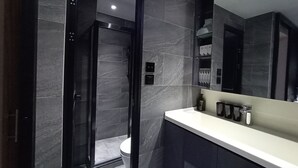 A modern bathroom with a walk-in shower, dark marble tiles, a white sink, and a large mirror. - The Nap Mong Kok (Kowloon)